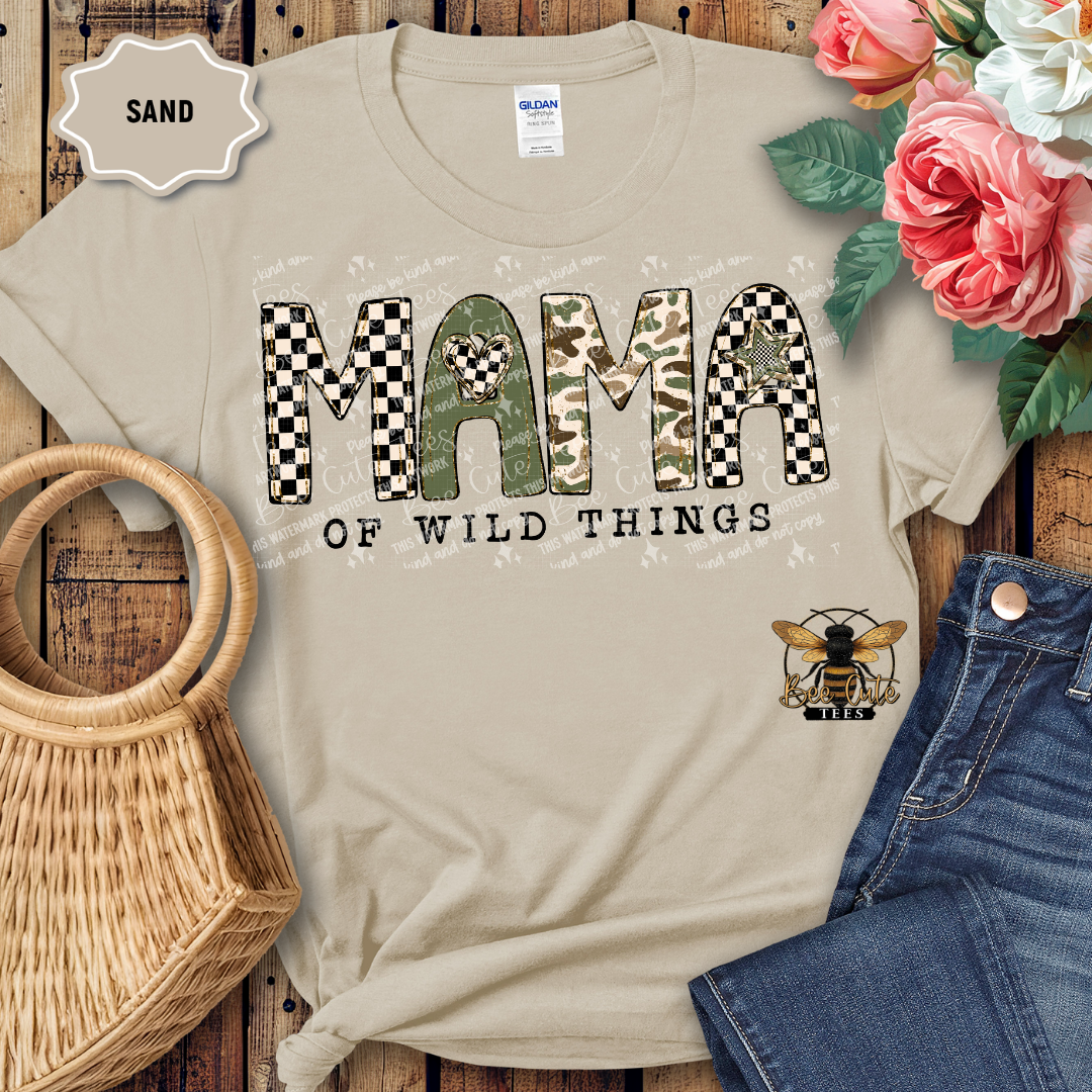 Beige t-shirt with 'Mama of Wild Things' text and bee logo on a wooden surface with flowers and denim jeans.