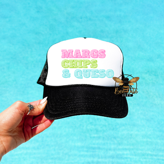 Trucker hat with 'MARGS CHIPS & QUESO' text held by a hand against a blue background