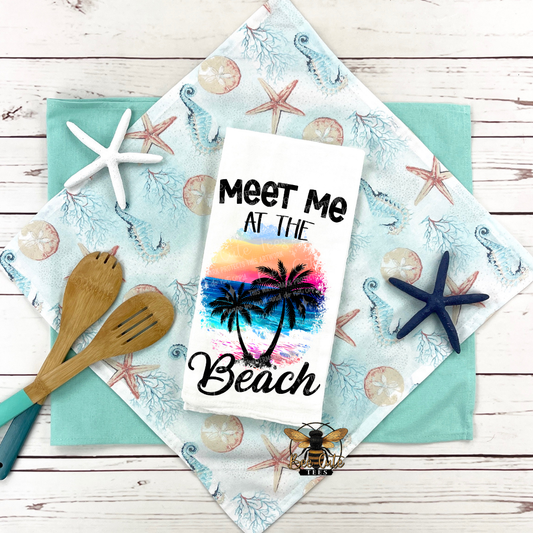 Kitchen towel with 'Meet Me at the Beach' text and palm tree design on a decorative cloth with starfish and seashells.