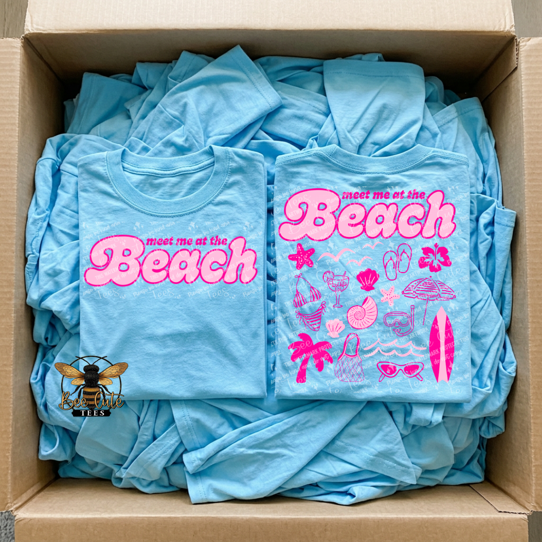 Box filled with blue t-shirts featuring 'Meet me at the Beach' design.