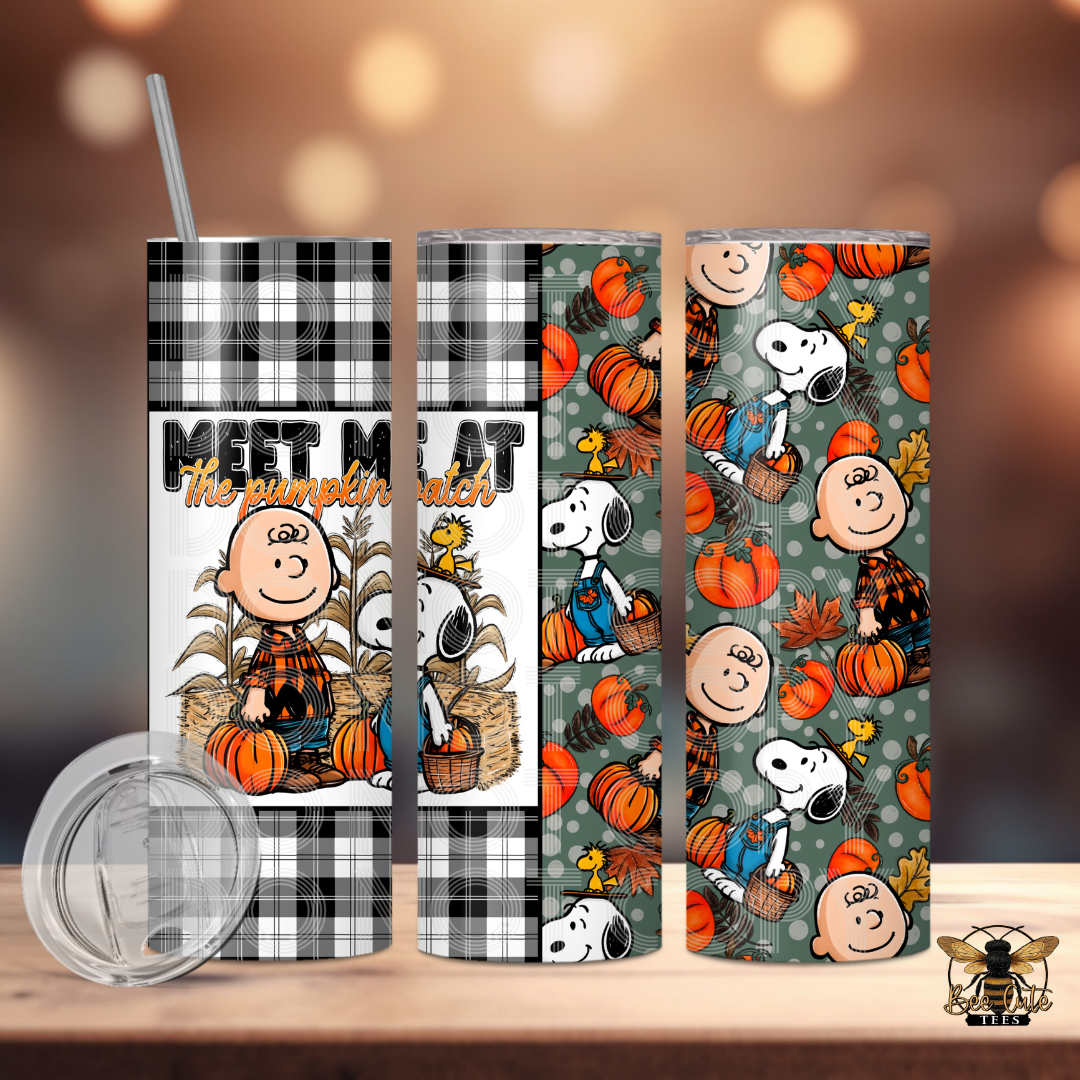 Three insulated tumblers with a fall-themed cartoon print are shown on a wooden surface against a blurred warm background. The tumblers feature black-and-white plaid, a white-and-gray plaid section, and a green pattern with pumpkins, leaves, and cartoon characters.