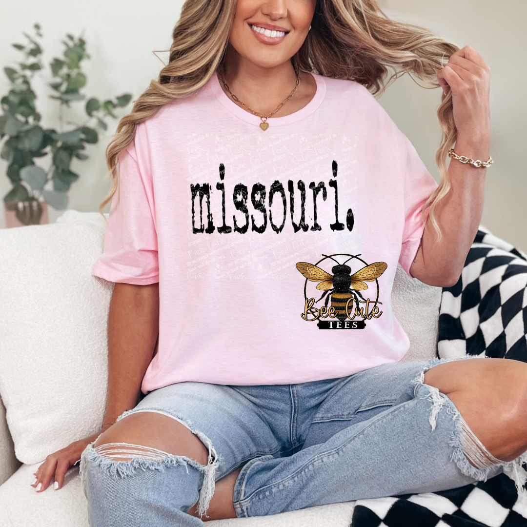 Woman wearing a pink t-shirt with 'missouri' and a bee logo, sitting on a couch.