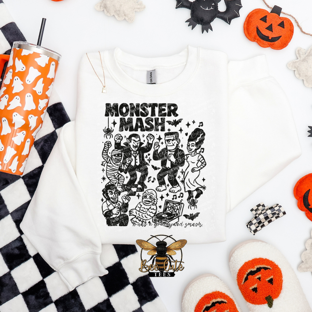 White t-shirt with 'Monster Mash' design, orange tumbler, and Halloween decorations on a white background