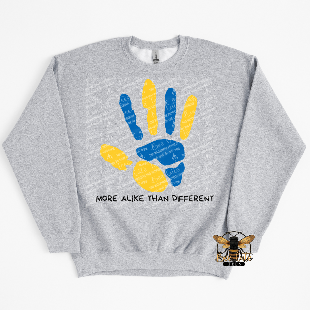 Gray sweatshirt with a colorful handprint design and text 'More Alike Than Different' on a white background.