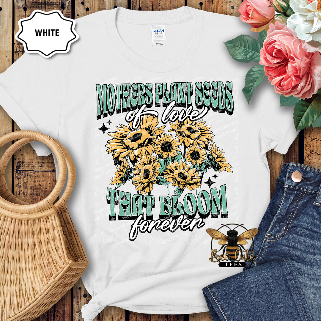 White t-shirt with sunflower design and text on a wooden surface with flowers and jeans.