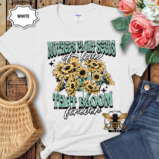 White t-shirt with sunflower design and text on a wooden surface with flowers and jeans.