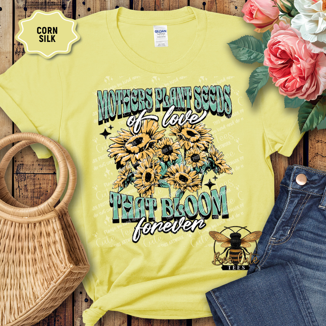 Yellow t-shirt with sunflower design and text on a wooden surface with flowers and jeans.