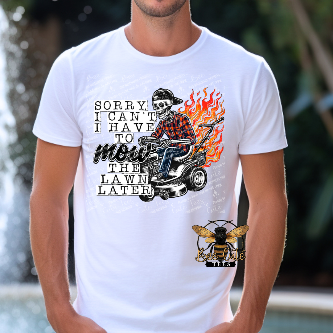 Man wearing a white graphic tee featuring a skeleton riding a lawn mower with flames behind it and the humorous phrase “Sorry, I Can’t, I Have to Mow the Lawn Later.”
