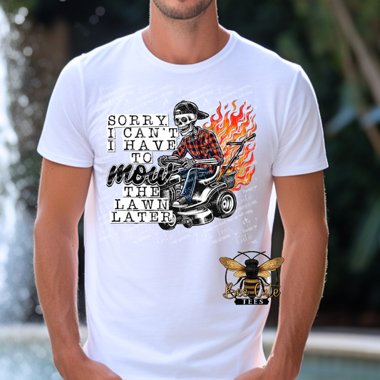 Man wearing a white graphic tee featuring a skeleton riding a lawn mower with flames behind it and the humorous phrase “Sorry, I Can’t, I Have to Mow the Lawn Later.”
