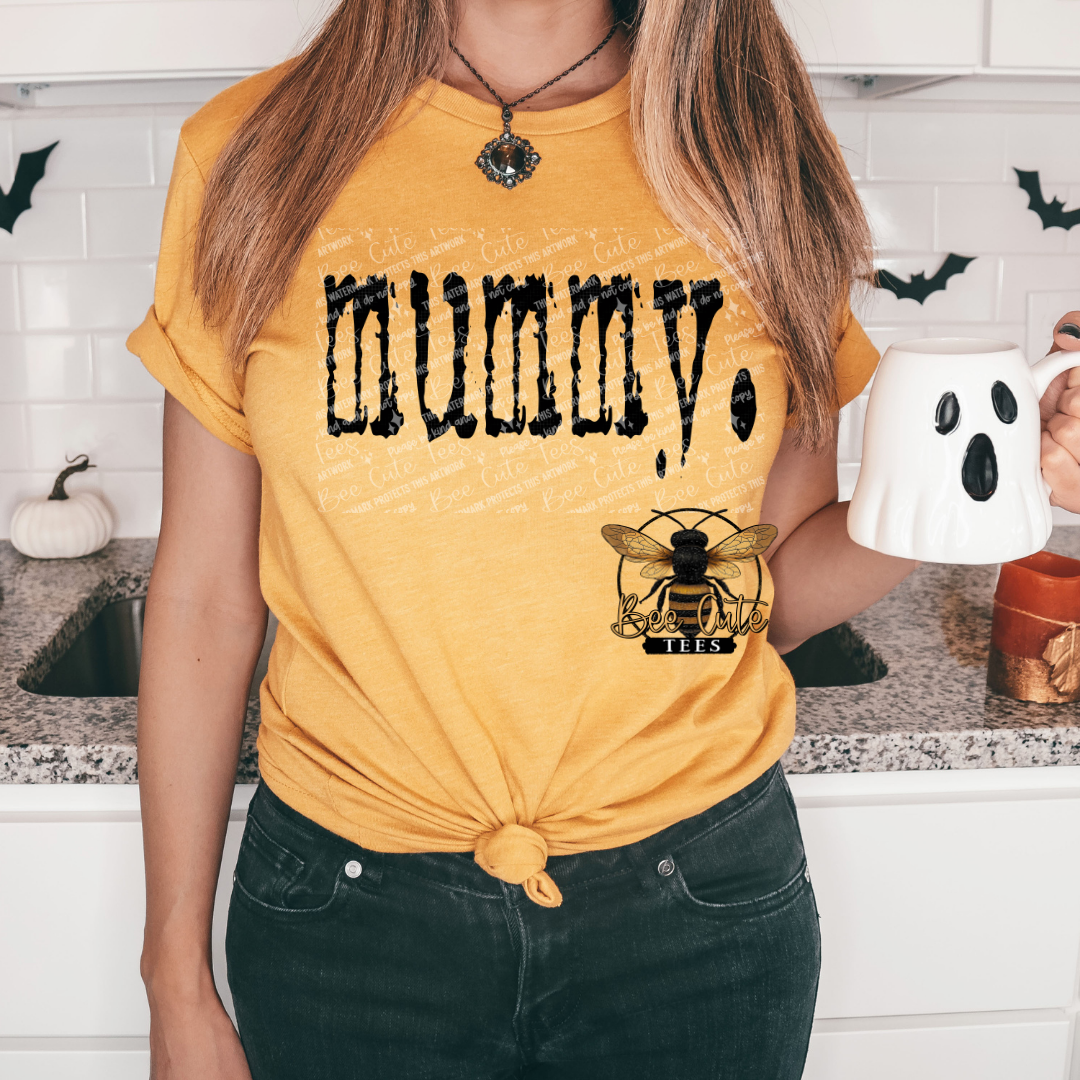 Person wearing a yellow t-shirt with 'Mummy' and a bee logo, holding a mug in a kitchen.