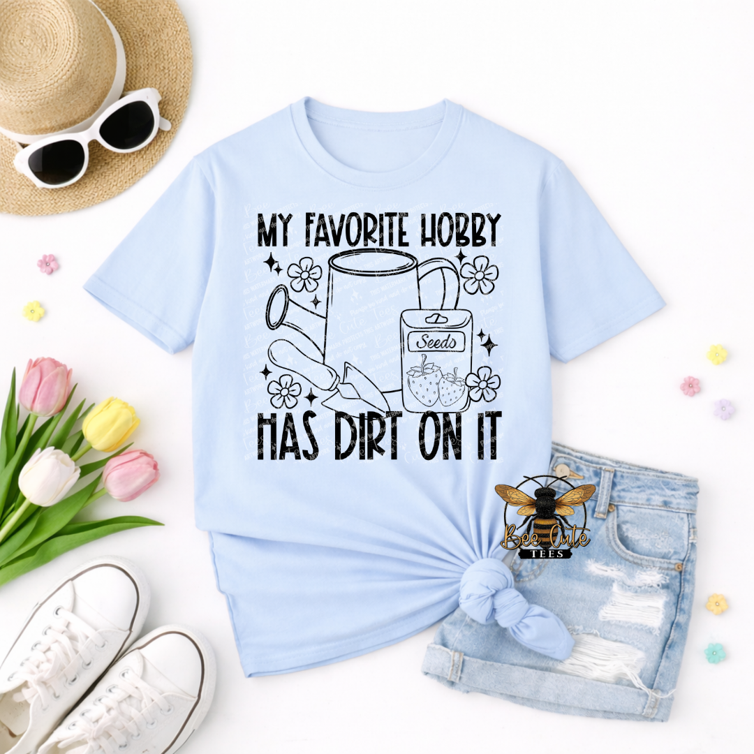Light blue t-shirt with gardening-themed design and text, surrounded by accessories on a white background.