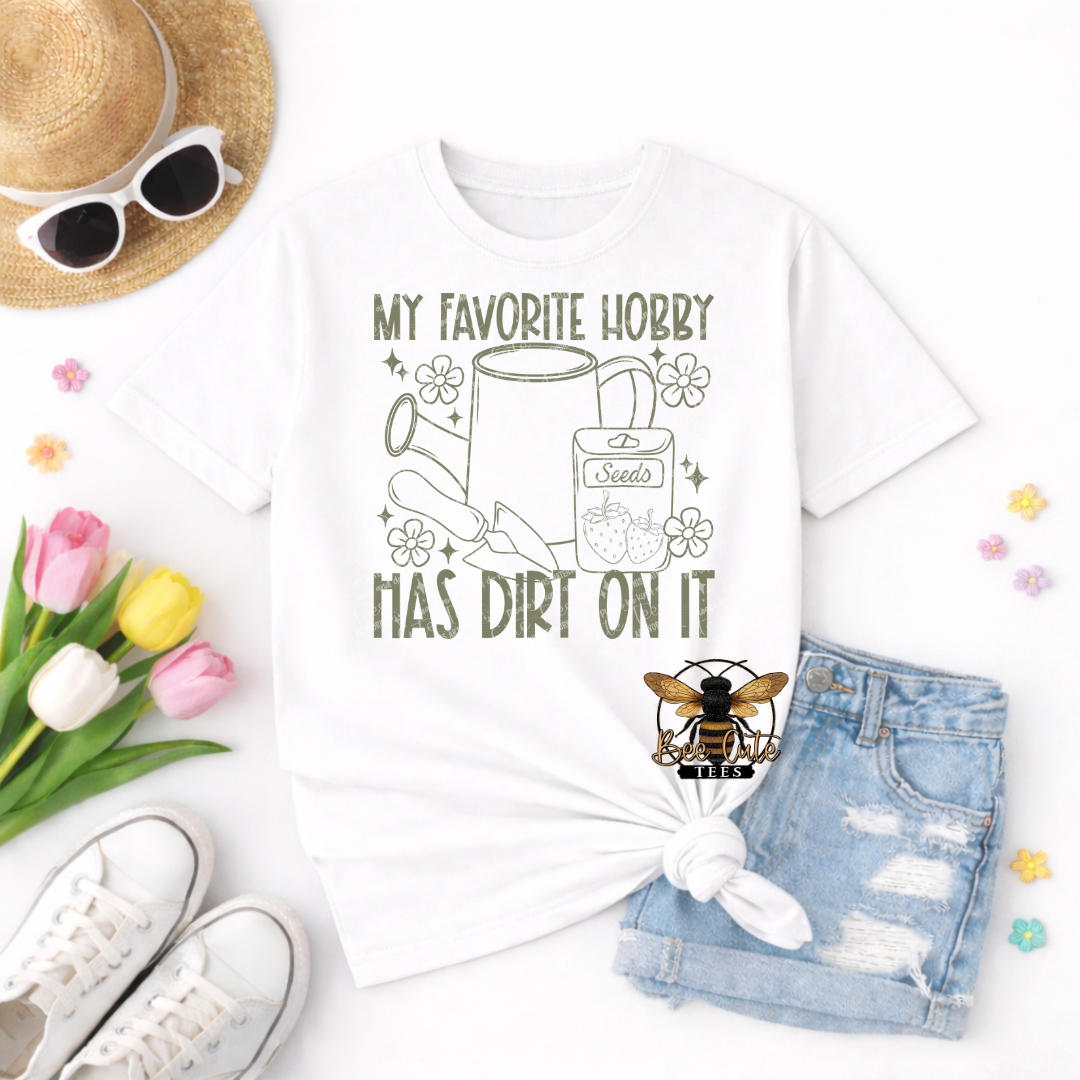 White t-shirt with 'My favorite hobby has dirt on it' design, sunglasses, tulips, and denim shorts on a white background