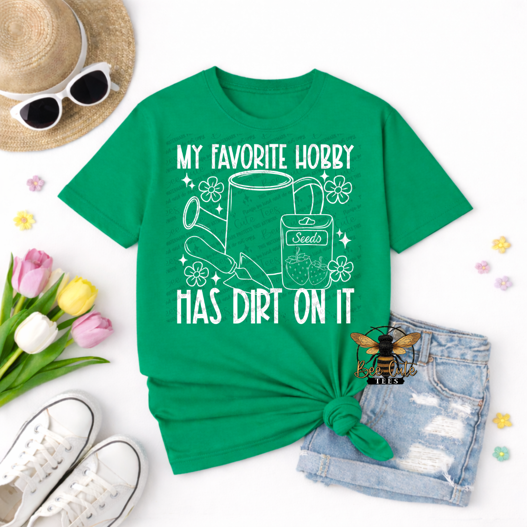 Green t-shirt with 'My favorite hobby has dirt on it' design, sunglasses, hat, shoes, and flowers on a white background