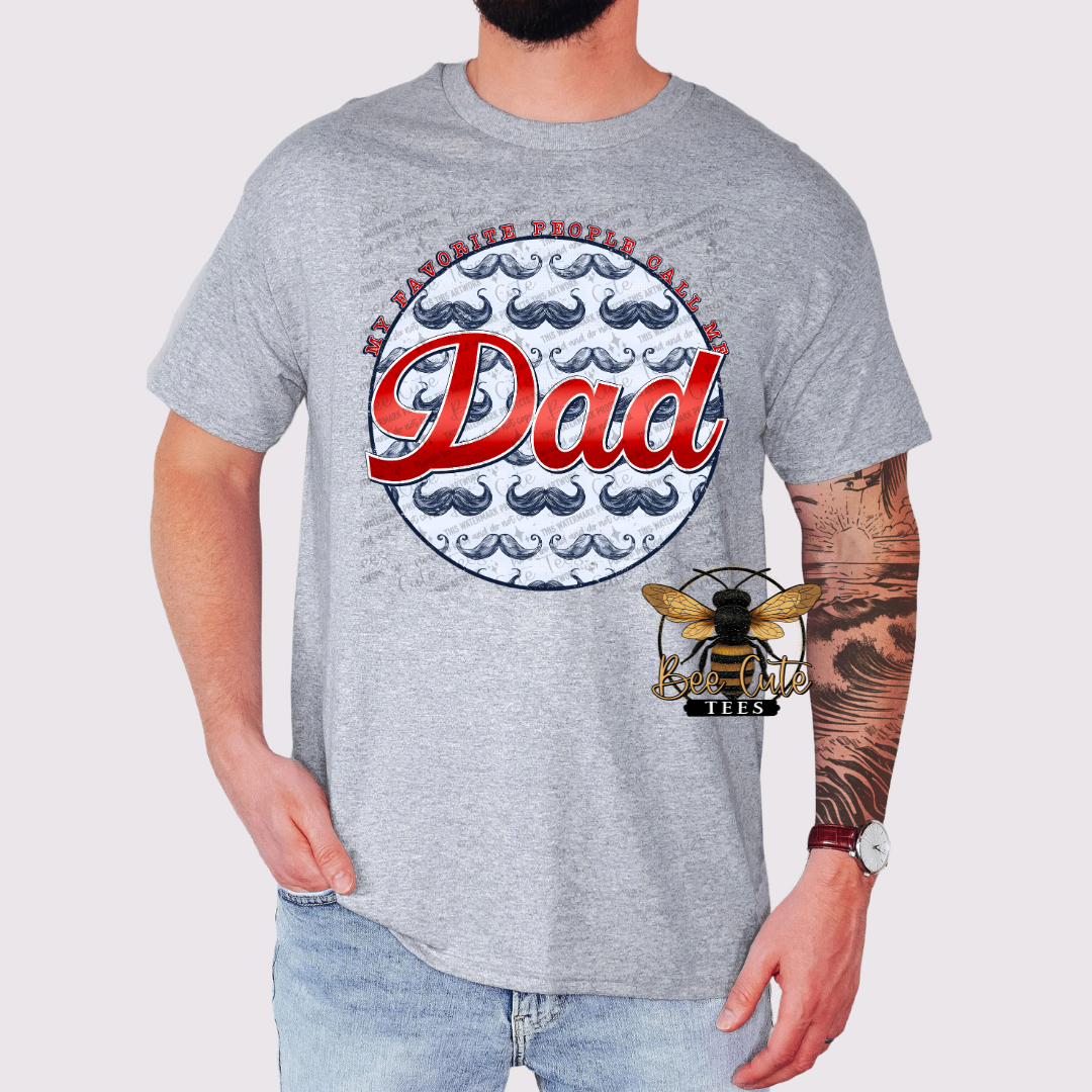 Gray graphic t-shirt worn by a man, featuring a circular design with mustaches and the phrase “My favorite people call me Dad” in bold red lettering.
