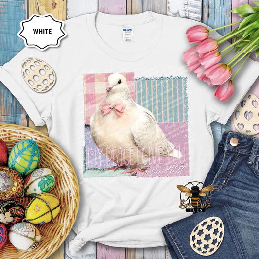 White t-shirt with a dove graphic and text, surrounded by Easter decorations on a wooden surface.
