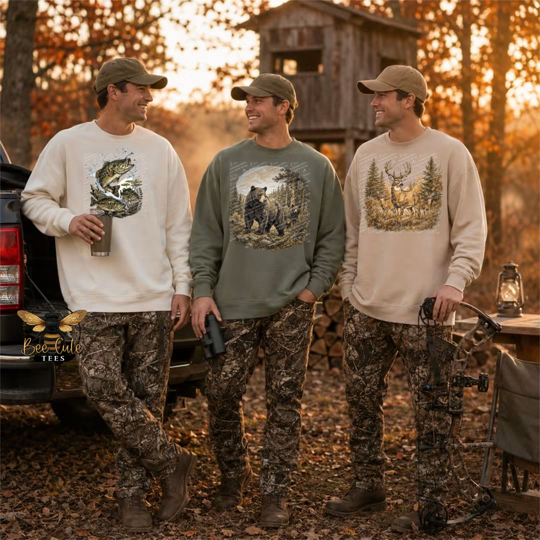 Three men standing outdoors in a wooded setting at sunset, each wearing a long-sleeve camouflage sweatshirt with a different hunting-themed graphic: a fish, a bear, and a deer. One man holds a bow, and the scene includes a truck, treehouse, and outdoor gear.