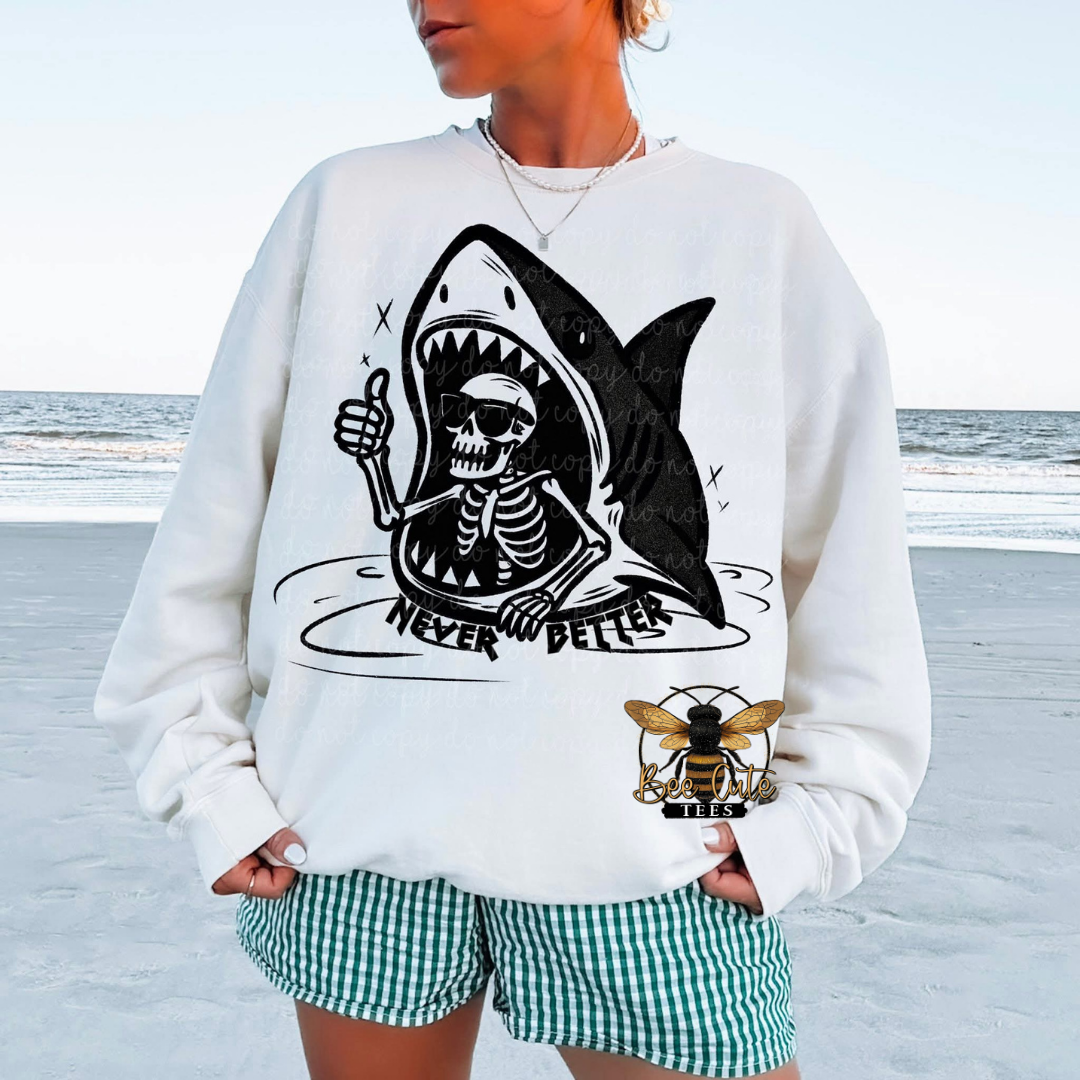 Person wearing a white sweatshirt with a shark skeleton design on a beach.