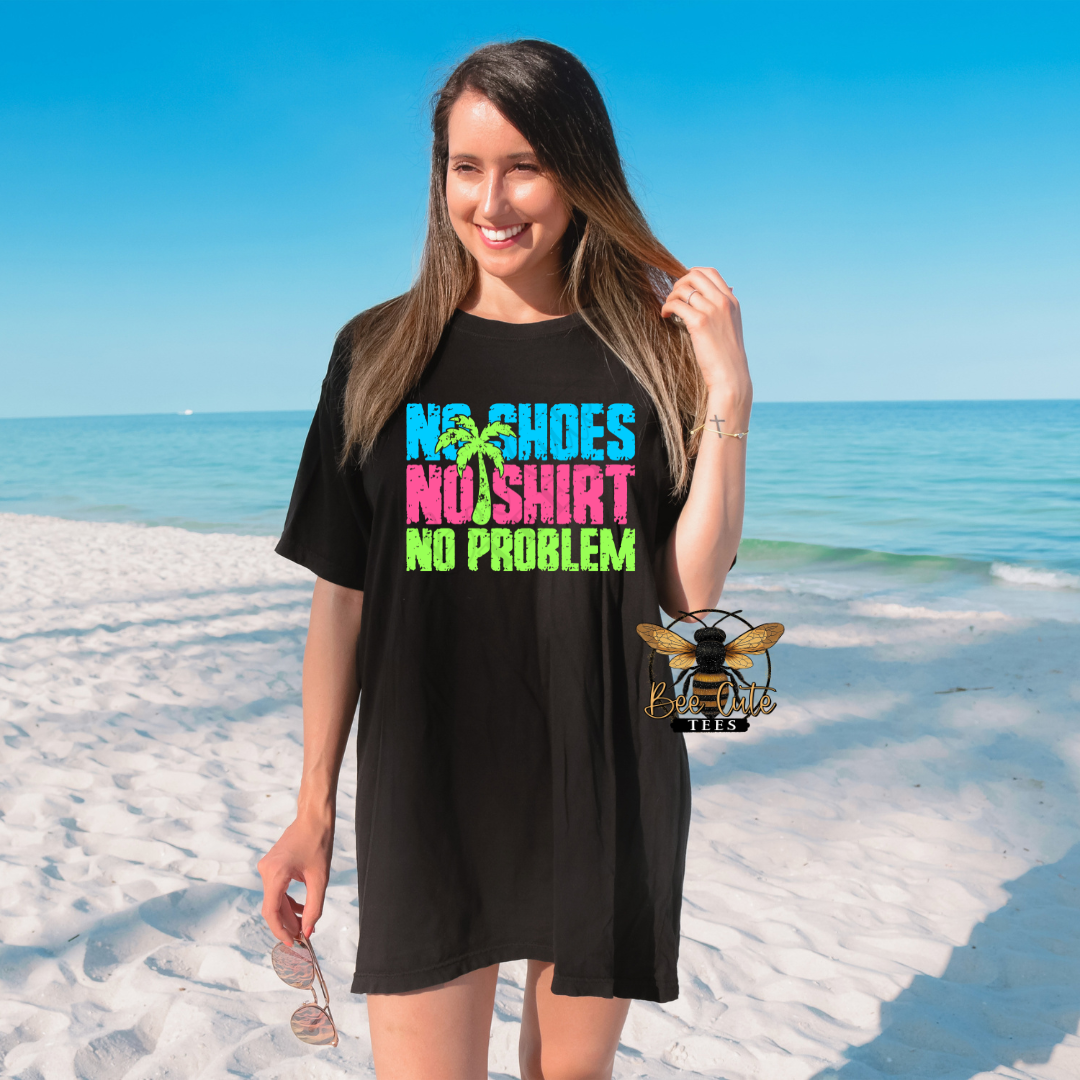 Woman wearing an oversized black graphic tee on a sunny beach with colorful neon text that reads “No Shoes No Shirt” paired with palm tree graphics and reflective sunglasses.