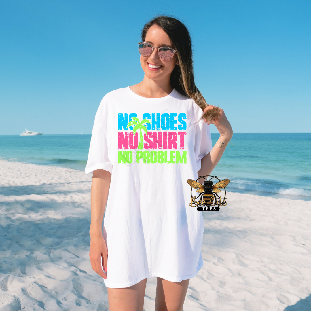 Woman wearing an oversized white graphic tee on a sunny beach with colorful neon text that reads “No Shoes No Shirt” paired with palm tree graphics and reflective sunglasses.
