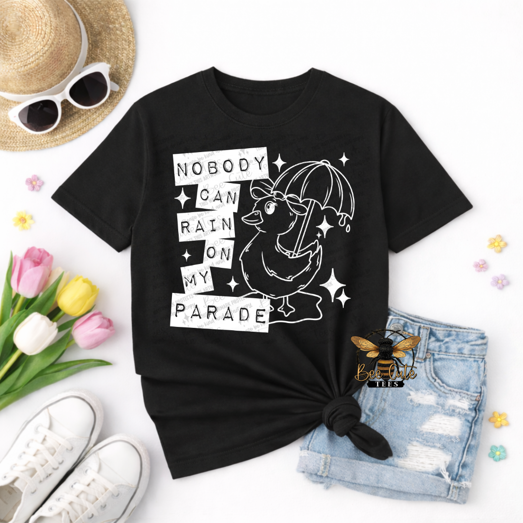 Black t-shirt with a graphic design and text, placed on a white surface with accessories like sunglasses, tulips, and shorts.