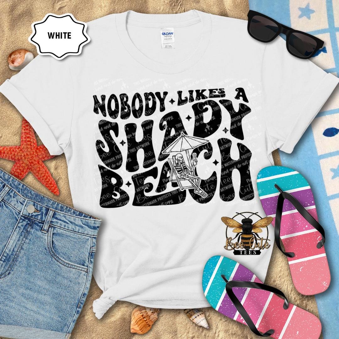 White t-shirt with 'Nobody Likes a Shady Beach' text, sunglasses, and flip-flops on a beach-themed background.