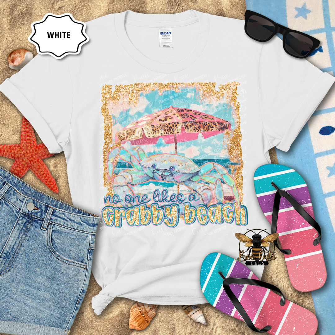White t-shirt with beach-themed design and text, surrounded by beach accessories on a sandy background.
