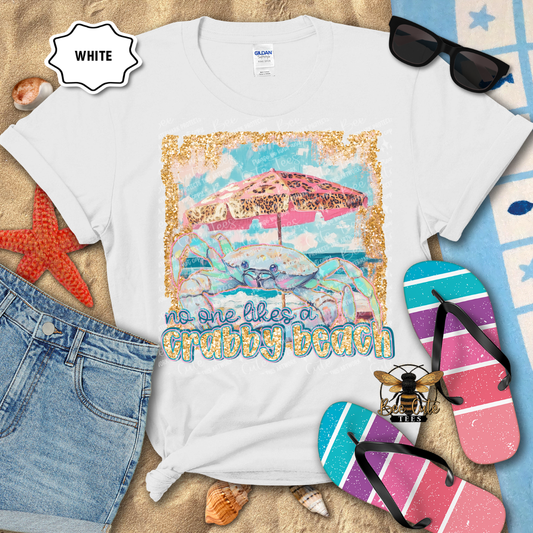 White t-shirt with beach-themed design and text, surrounded by beach accessories on a sandy background.