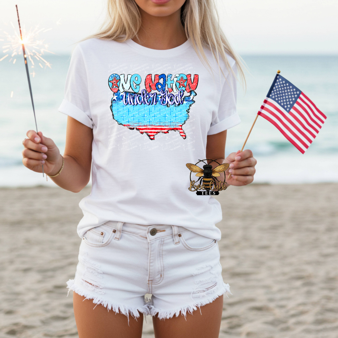 Person on a beach wearing a white t-shirt with a colorful graphic and holding an American flag and sparkler.