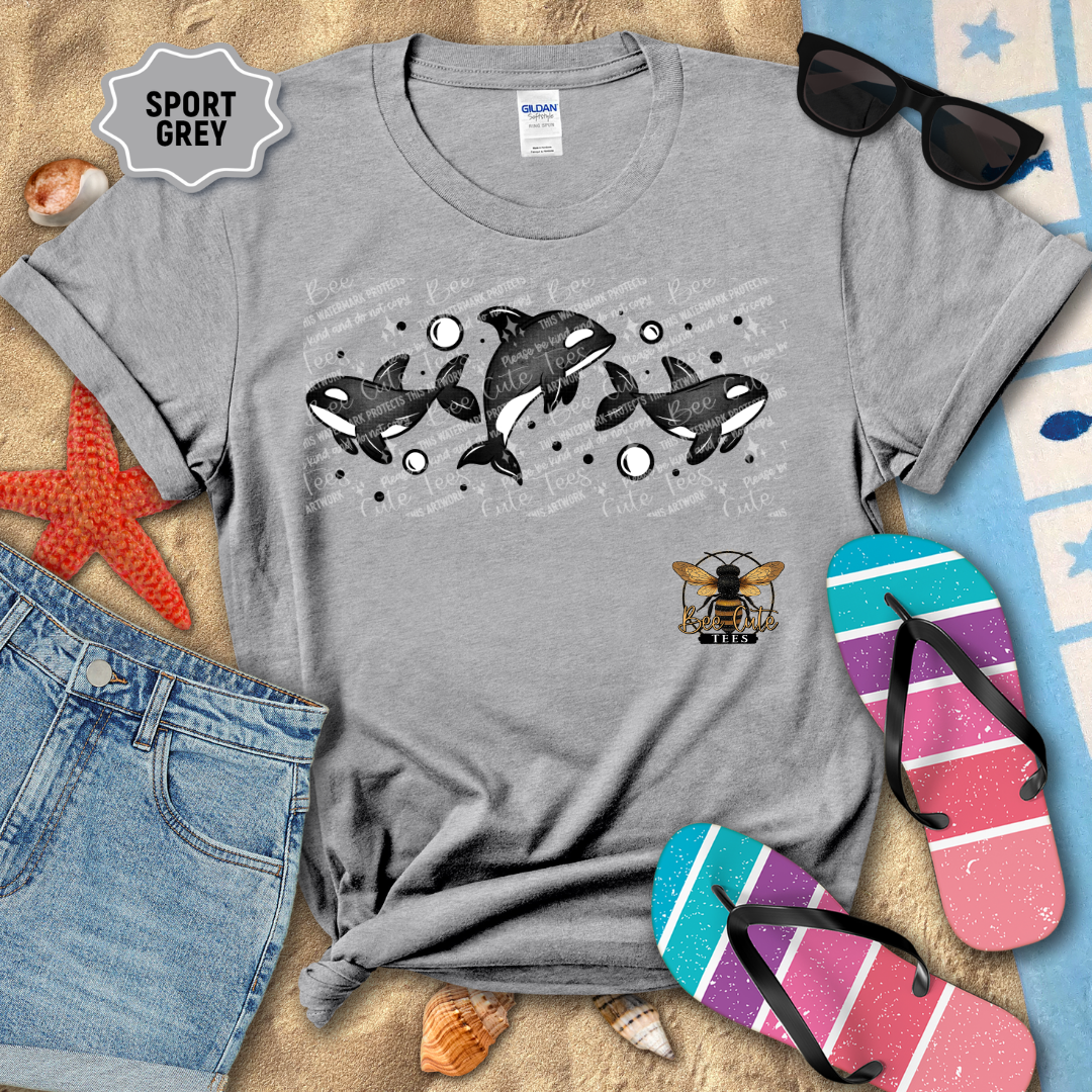 Gray t-shirt with whale design on a sandy surface with beach accessories.