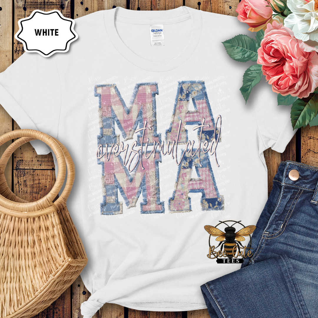 White t-shirt with floral 'MAMA' design on a wooden surface with flowers and jeans.