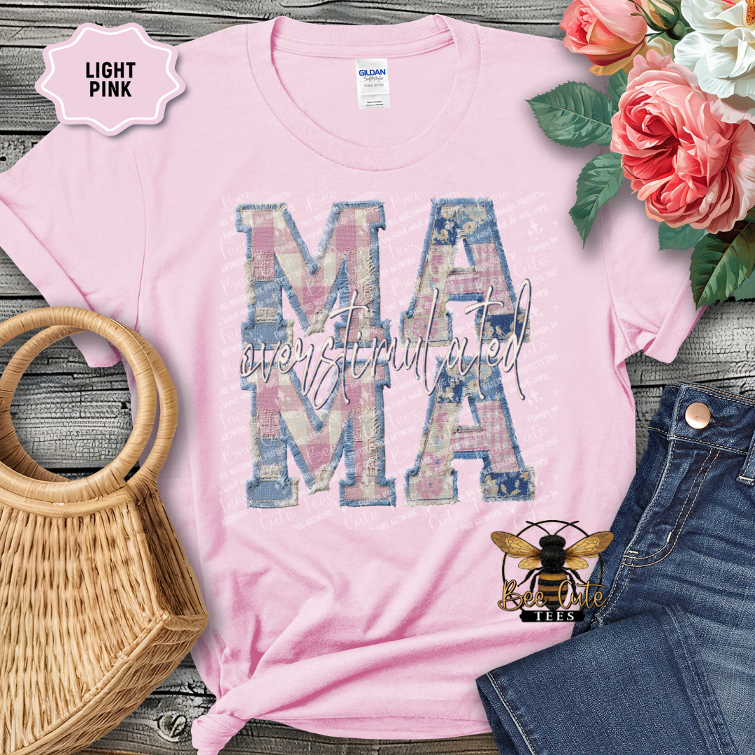 Light pink t-shirt with 'MAMA' design, surrounded by flowers and denim jeans on a wooden surface.