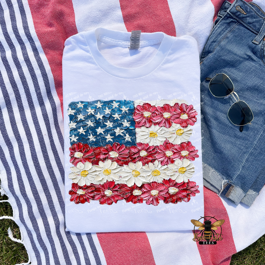 White t-shirt with American flag design made of flowers on a red and white striped fabric background.