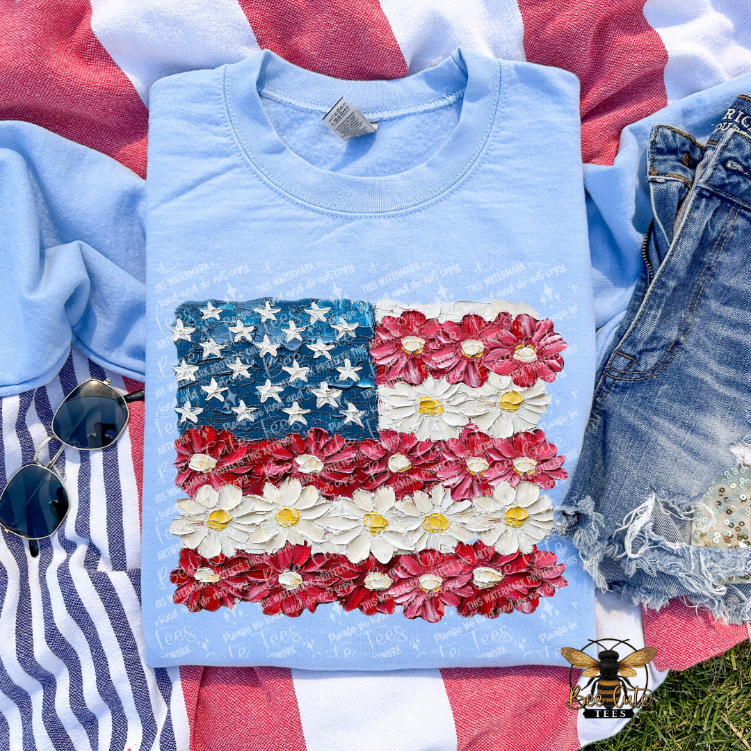 Light blue t-shirt with American flag design made of flowers on a grassy background