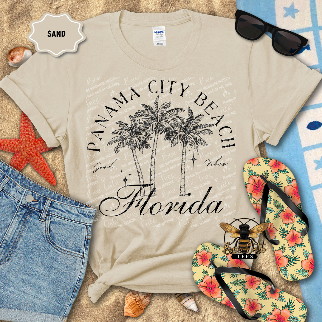 Beige t-shirt with 'Panama City Beach, Florida' design on a sandy background with flip-flops and sunglasses.