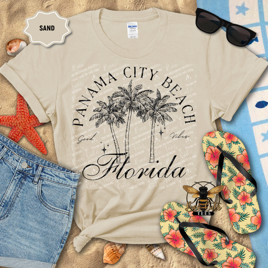 Beige t-shirt with 'Panama City Beach, Florida' design on a sandy background with flip-flops and sunglasses.