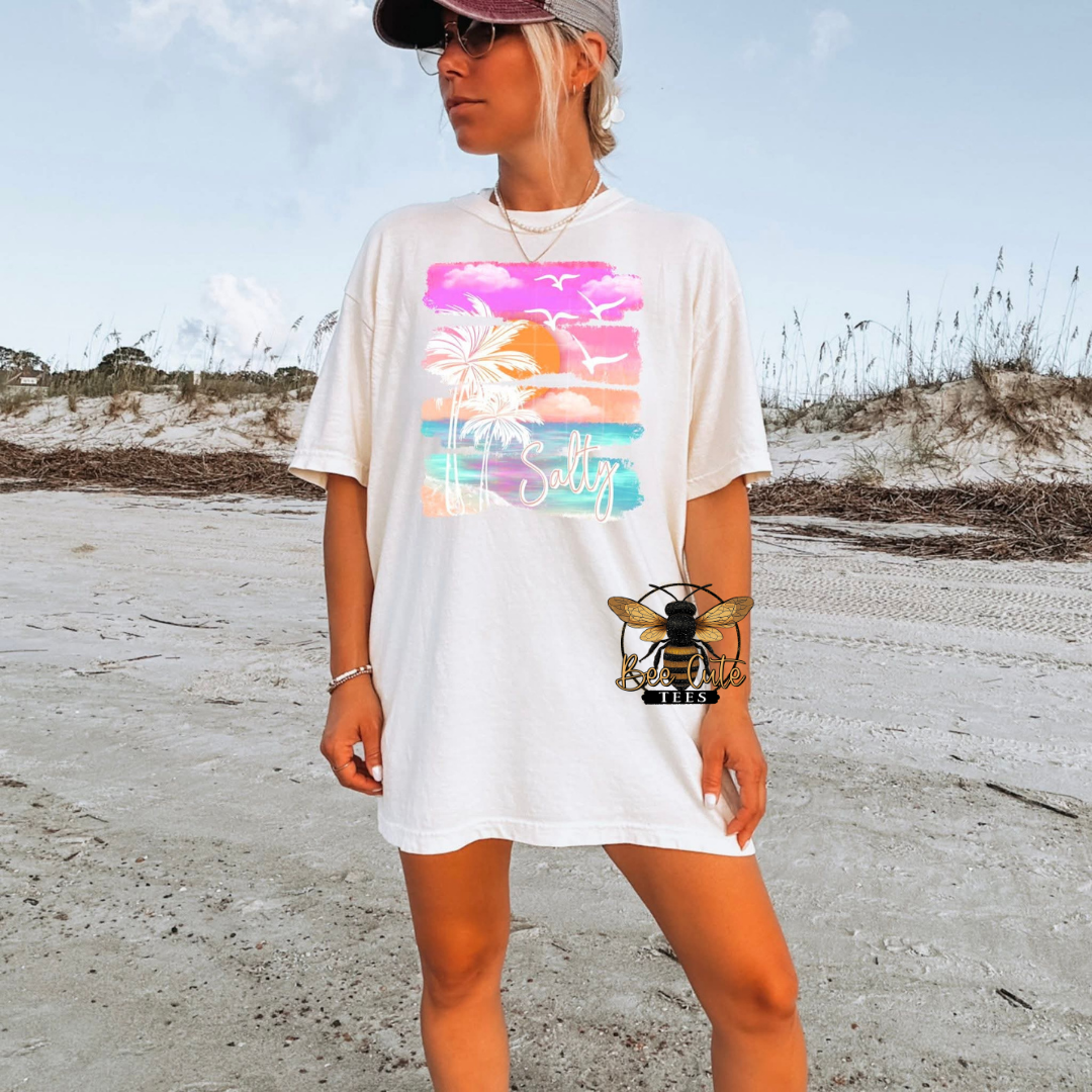 Person wearing a white t-shirt with a colorful graphic on a beach
