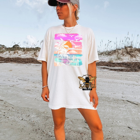 Person wearing a white t-shirt with a colorful graphic on a beach