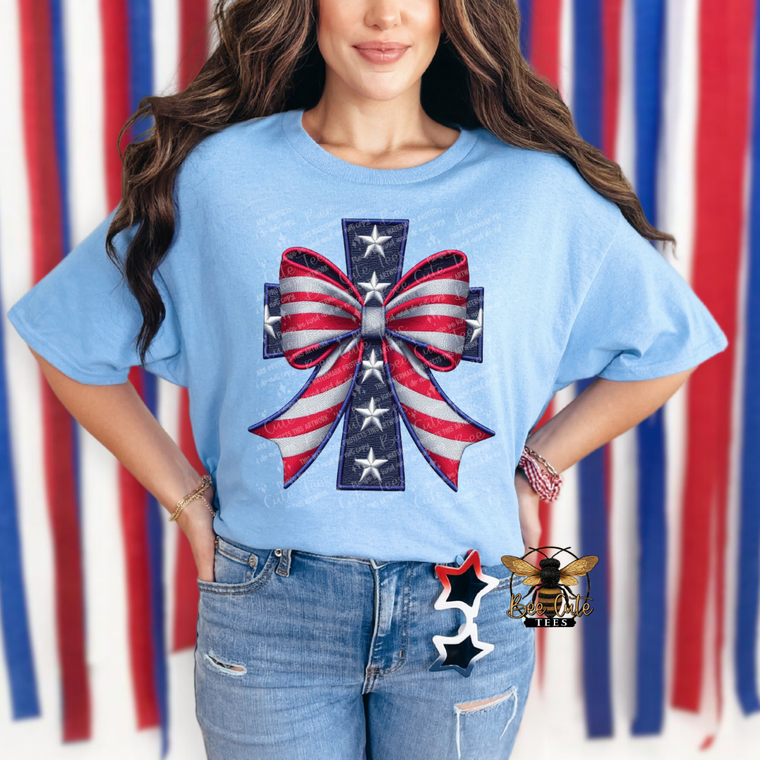 Woman wearing a blue t-shirt with a red, white, and blue bow design against a striped background.