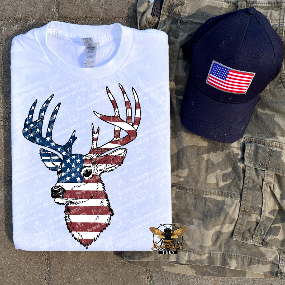 White t-shirt with deer design, navy cap with American flag, and camouflage shorts on a textured surface.