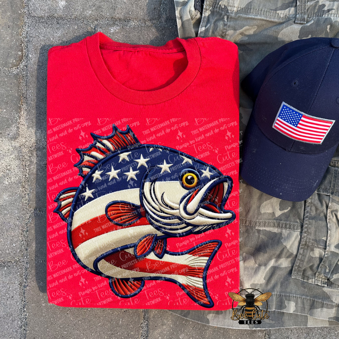 Red t-shirt with fish design and American flag, navy cap with flag patch on gray pavement.