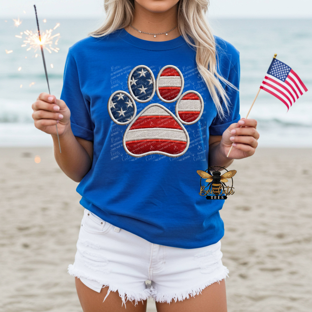 Person wearing a blue t-shirt with an American flag paw print design on a beach.