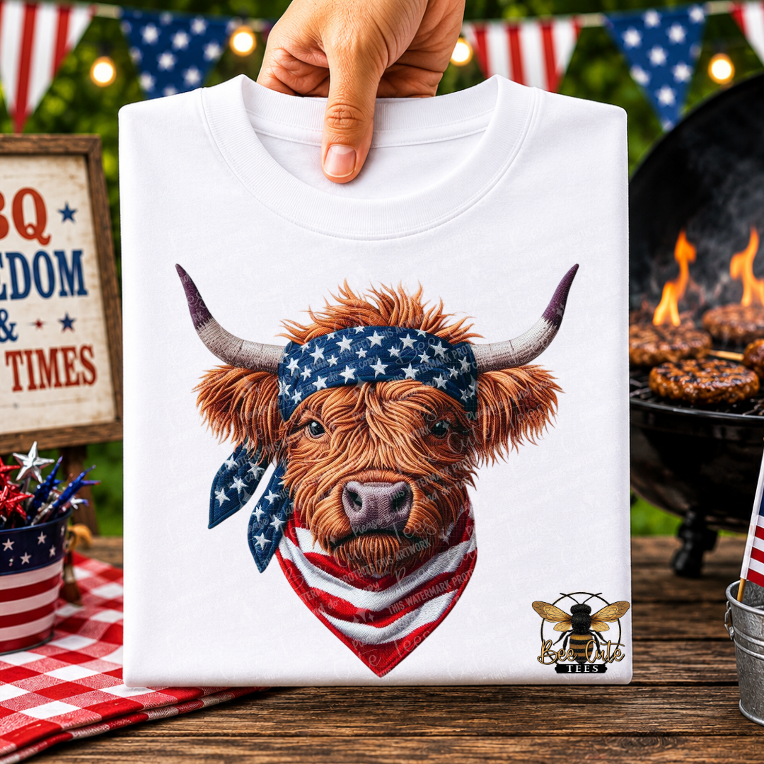 White t-shirt with a cow wearing an American flag bandana held by a hand, with a grill and flags in the background.