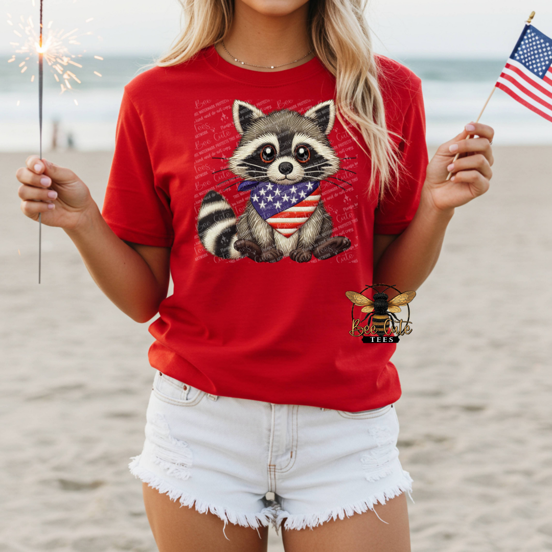 Person wearing a red t-shirt with a raccoon graphic holding an American flag on a beach.