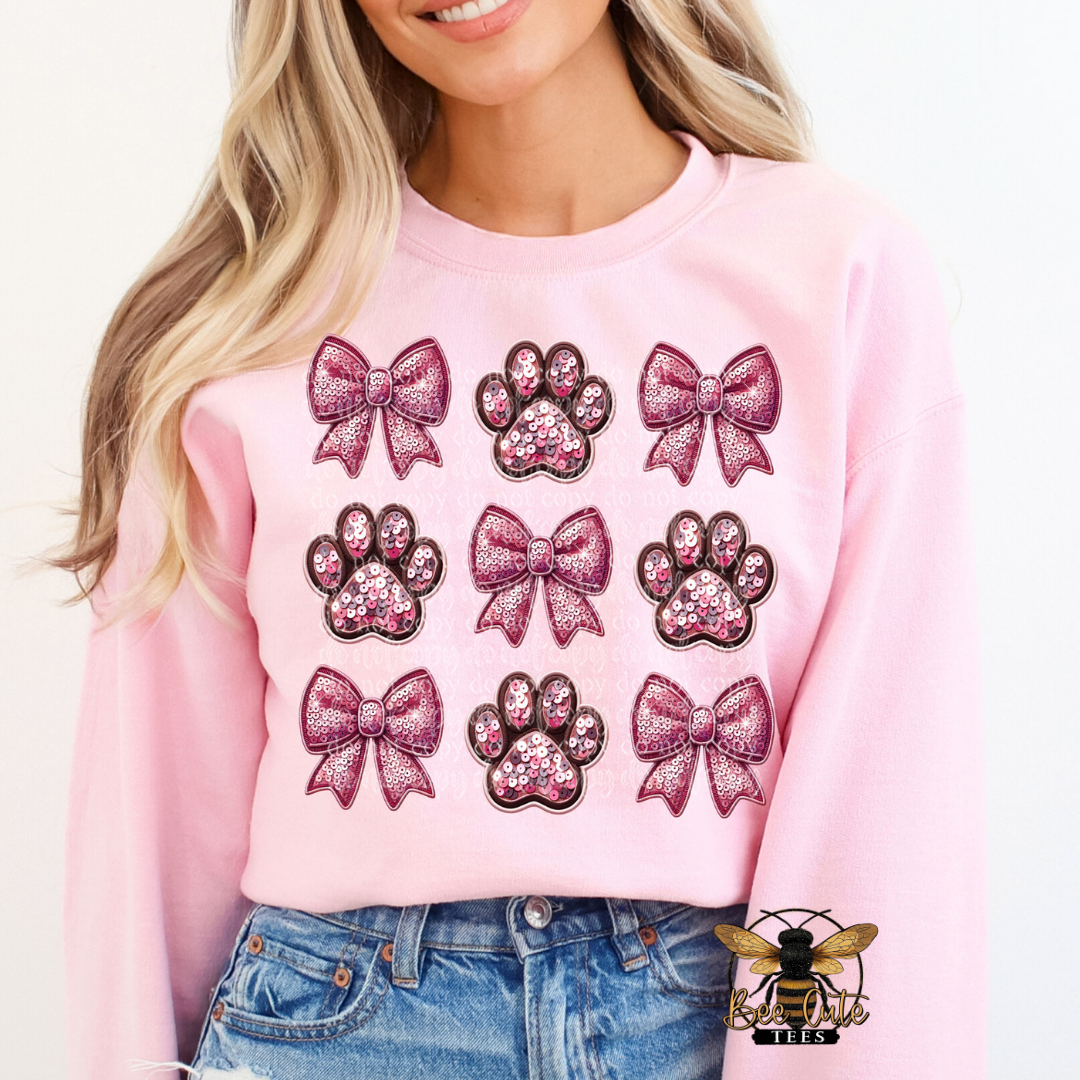 Person wearing a pink sweatshirt with glittery bow and paw print designs.