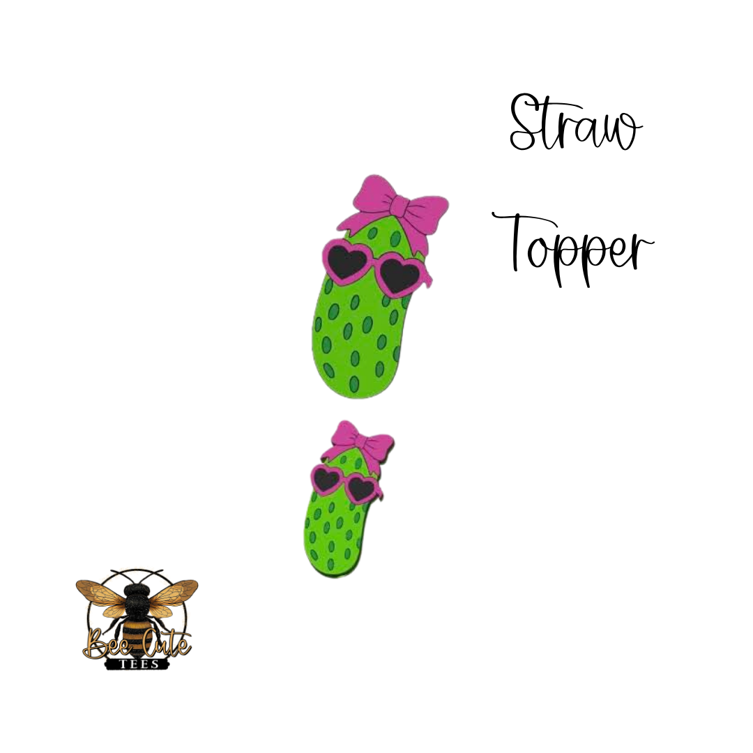Two green straw toppers with pink bows and sunglasses on a white background, featuring a logo at the bottom left corner.
