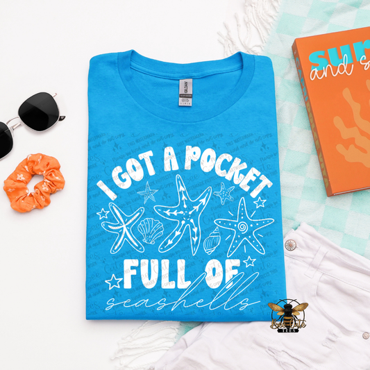 Blue t-shirt with beach-themed design and accessories on a light blue background