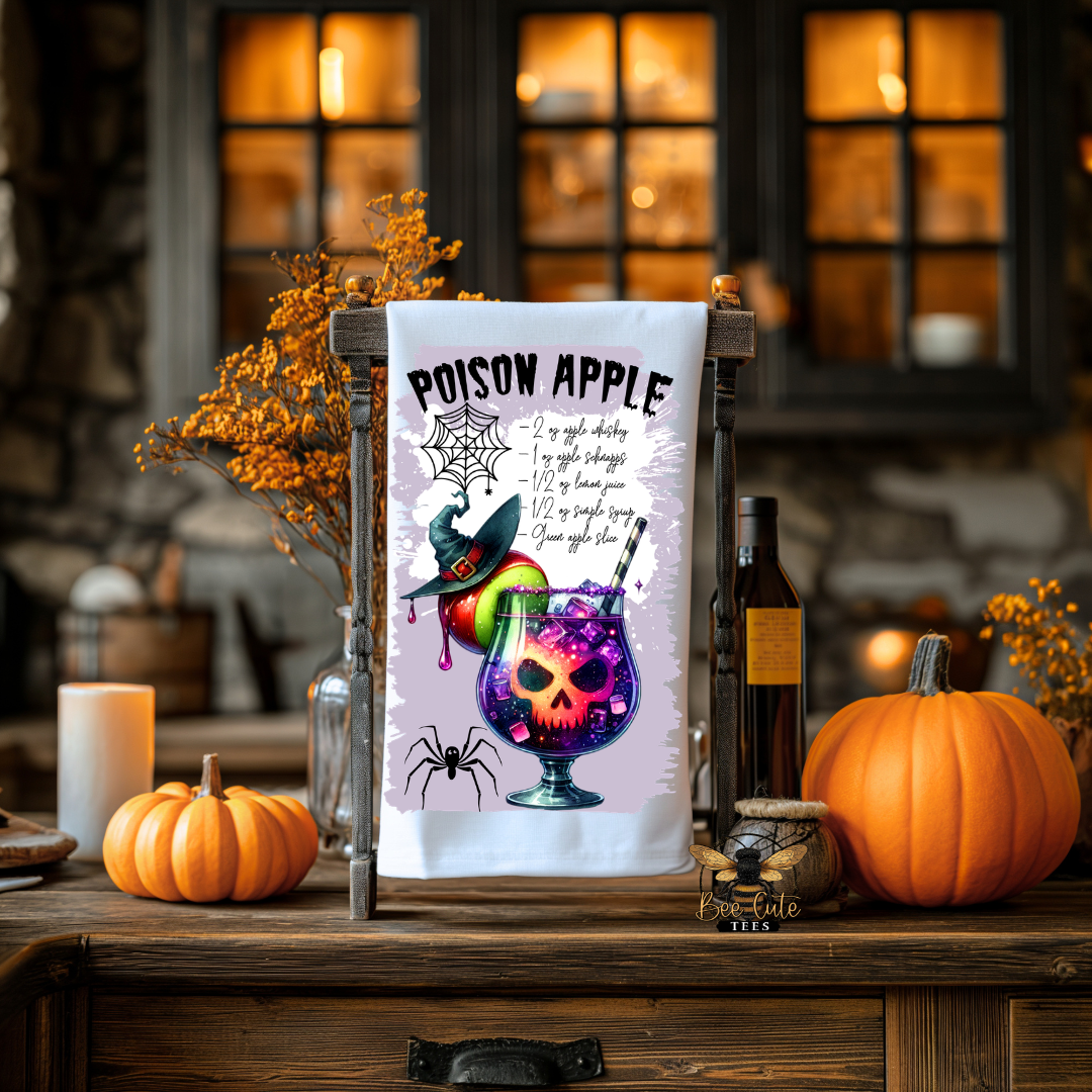 A Halloween-themed decorative tea towel with a 'Poison Apple' design, displayed on a wooden stand on a rustic wooden table surrounded by pumpkins, candles, and autumn decor.