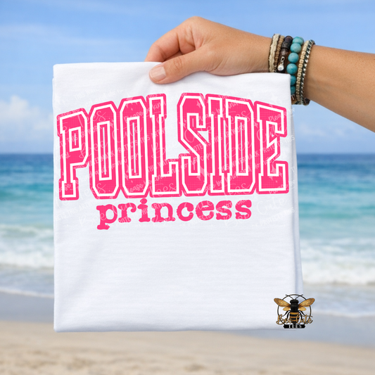 Hand holding a t-shirt with 'Poolside princess' text against a beach background