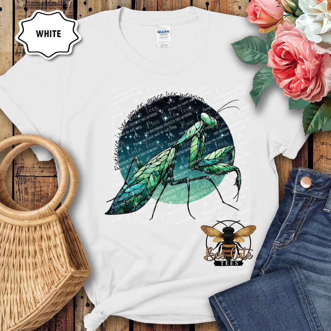 White t-shirt with praying mantis and bee logo on a wooden surface with flowers and jeans.