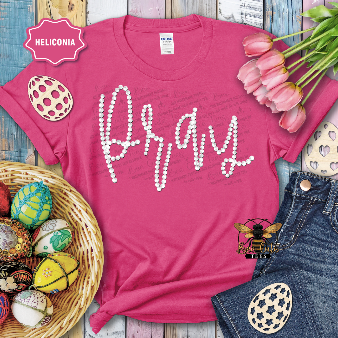 Pink t-shirt with 'Pray' text, Easter eggs, and tulips on a wooden surface.